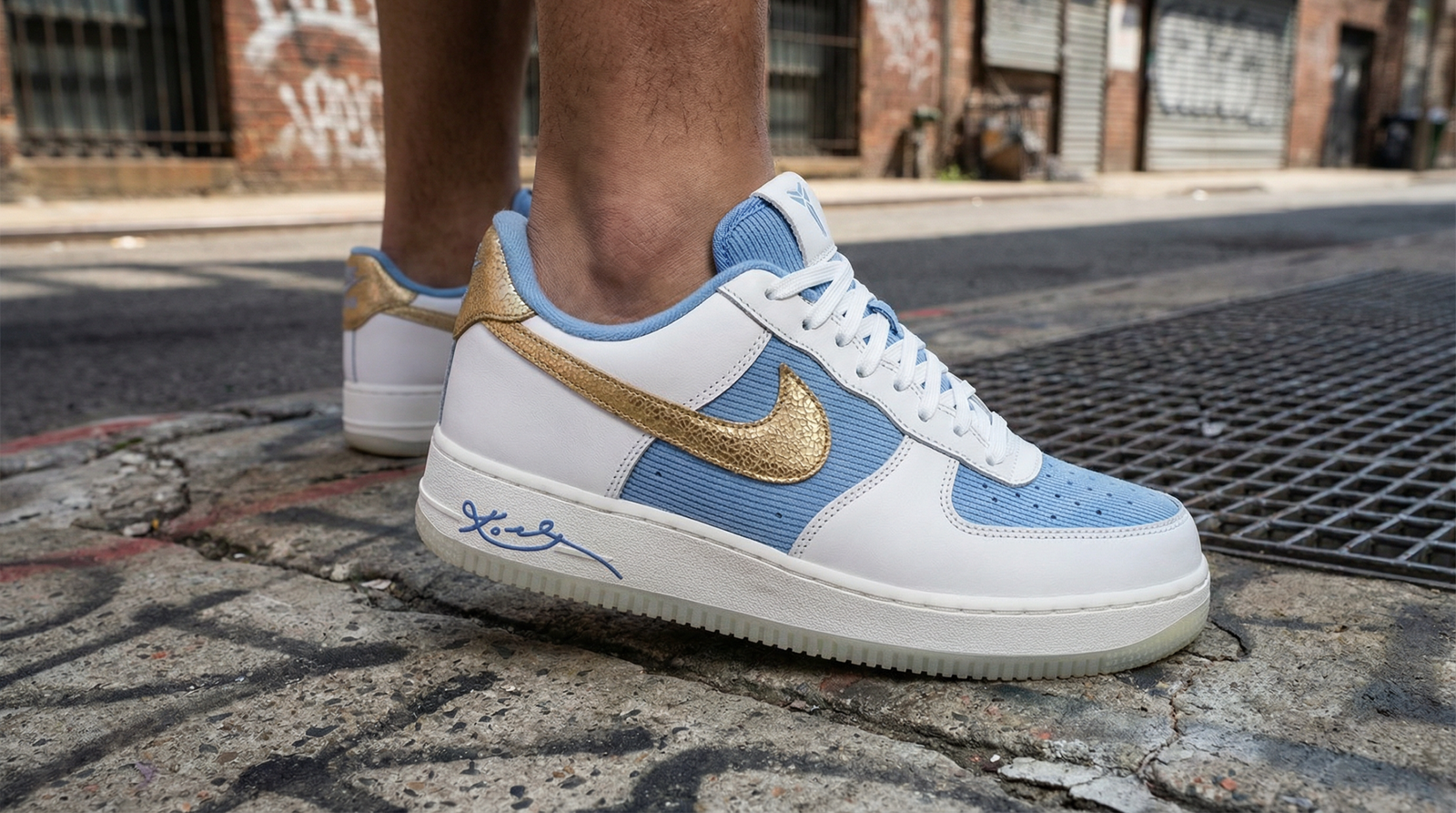 Edition Kobe Bryant Nike Air Force 1 'City of Champions', mesh Work Blue, détails Summit White et Metallic Gold, sur fond urbain.